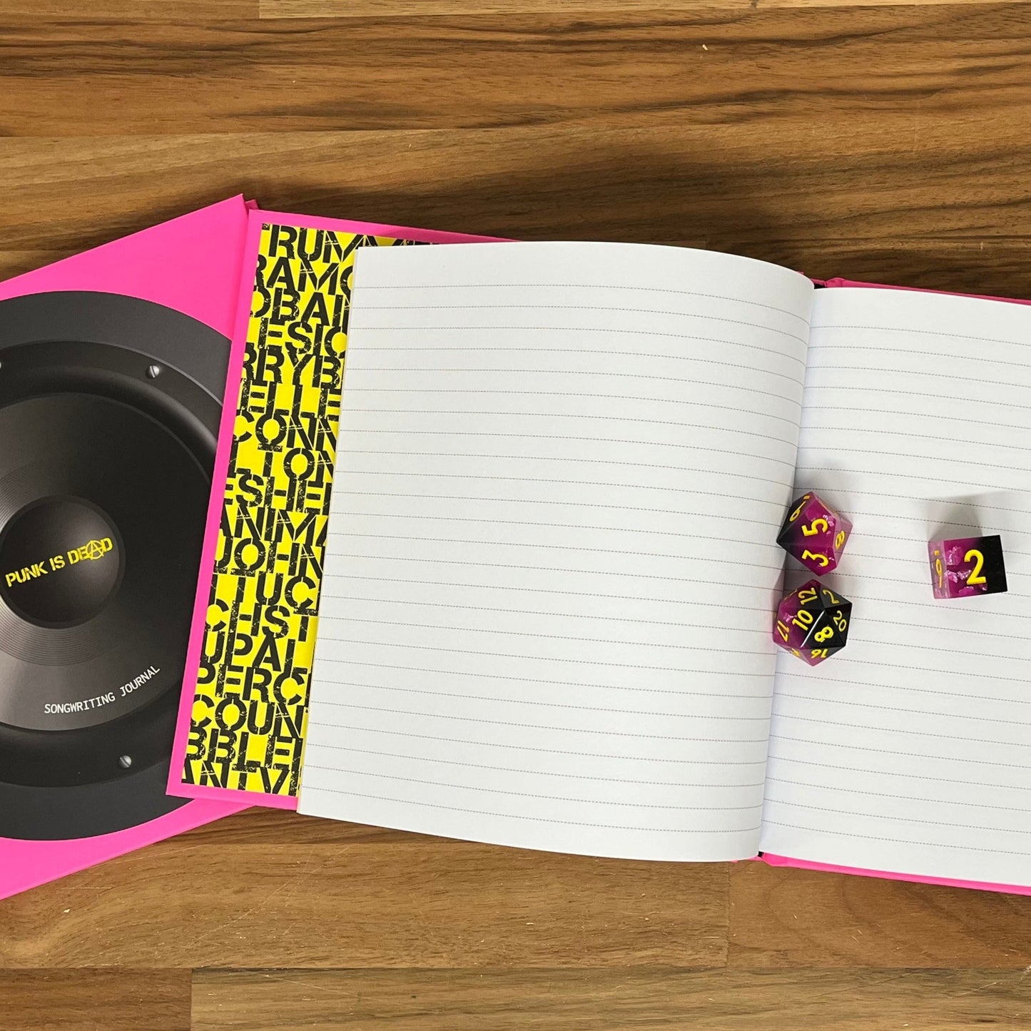Open notebook with dice and a pink and black object on a wooden surface